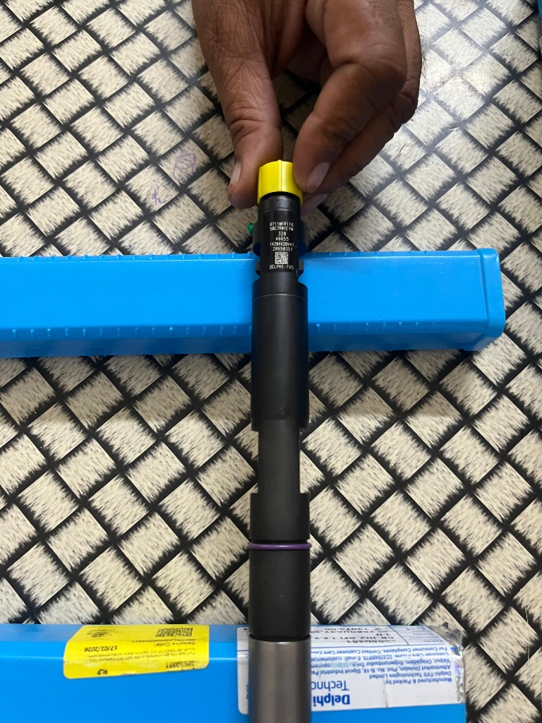 JCB 320/A6655 diesel fuel injector held over blue Delphi-TVS packaging showing 320 A6655 body markings — warehouse verification photo